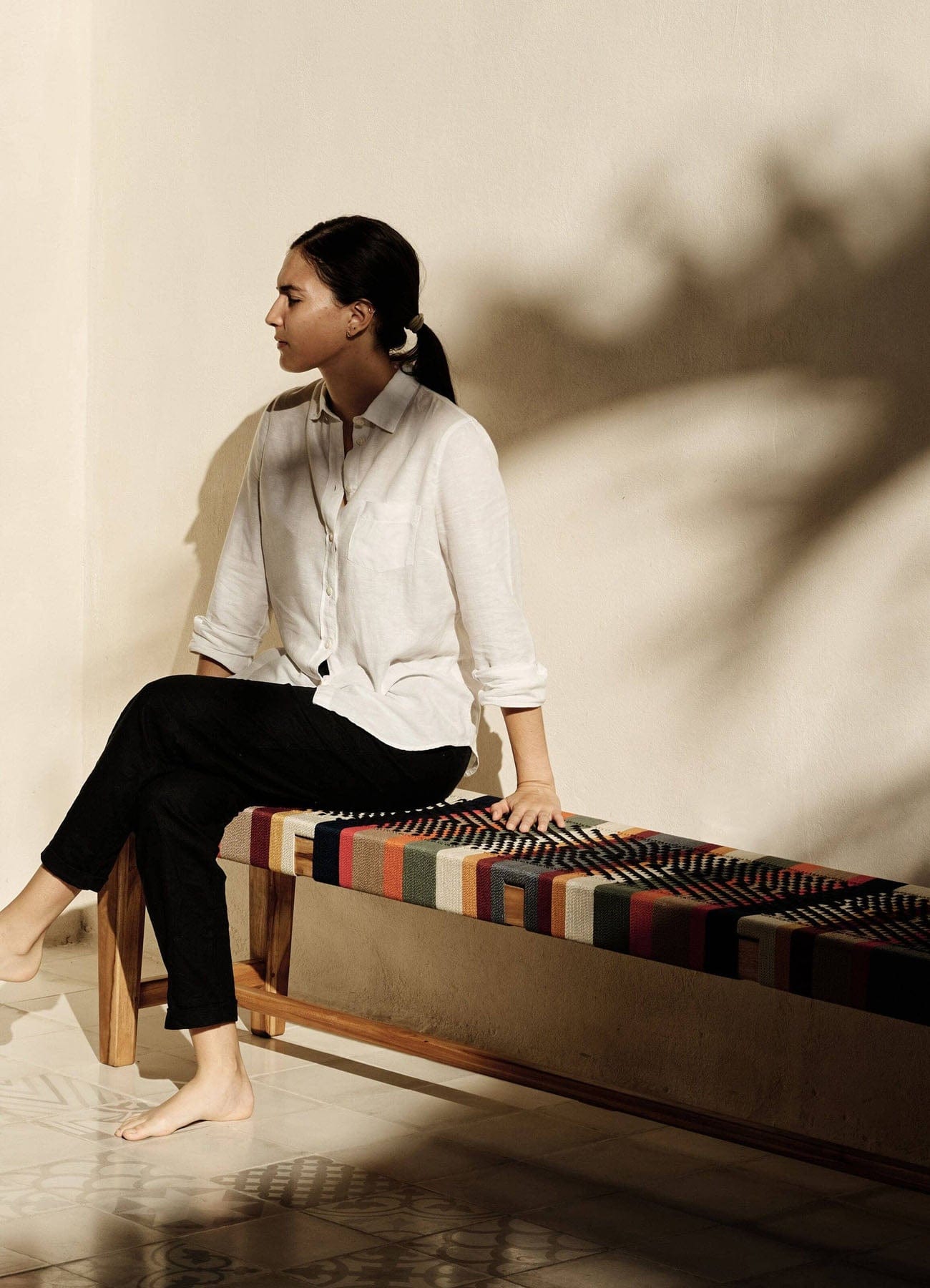 Woman sitting on a colorful bench woven against a neutral wall