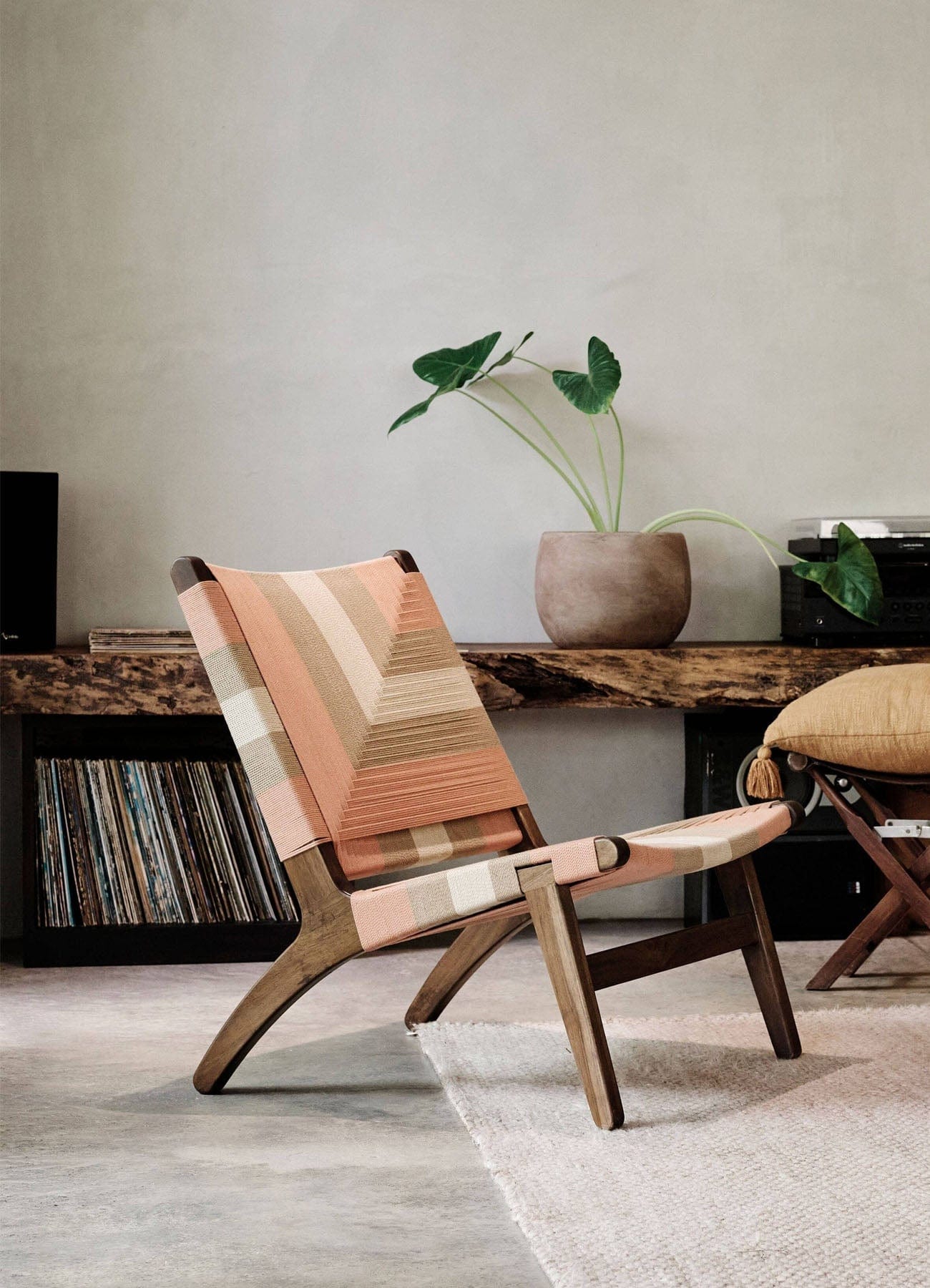 Modern lounge chair with woven rope back with muted pink colors in a room with a wooden desk and plants.