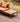Outdoor patio furniture set featuring a wooden coffee table with a geometric inlay pattern and a matching cushioned lounge chair in terracotta orange, set on a wooden deck with a blurred natural background.