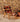 A mid-century modern wooden lounge chair with a woven geometric patterned seat and back, set against a rustic stone wall background.