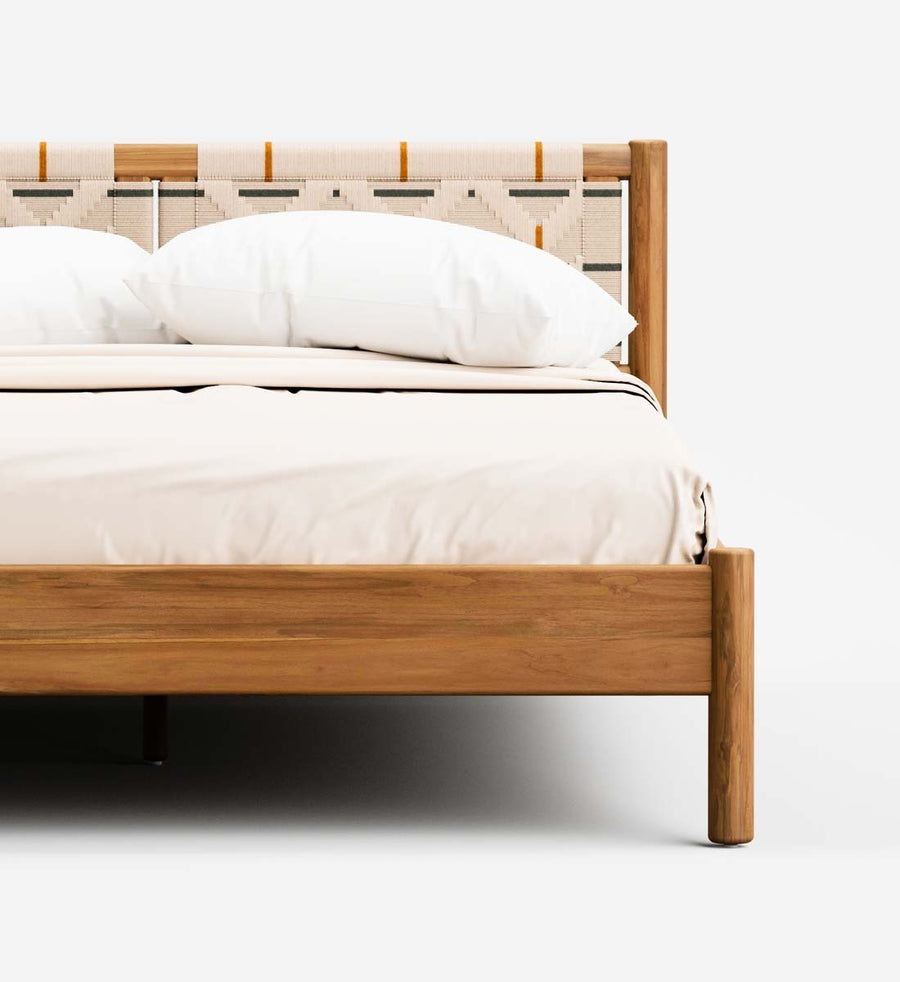 A close-up of a wooden bed frame with a woven headboard, dressed in white bedding and pillows, set against a clean white background.