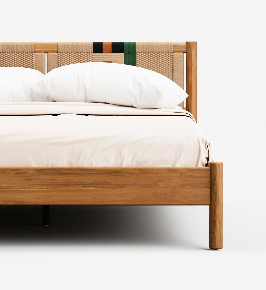 A close-up of a wooden bed frame with woven cane panels on the headboard and footboard, styled with white bedding and pillows against a clean white background.