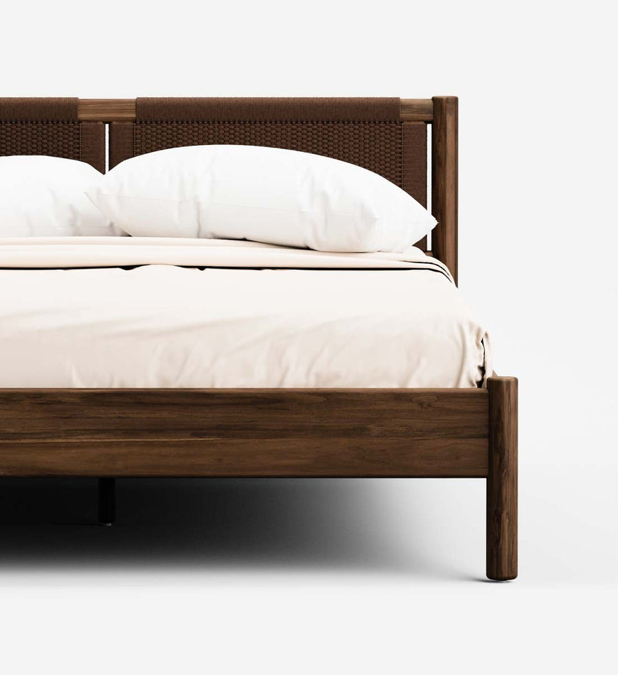 A close-up of a modern wooden bed frame with a woven cane headboard, dressed in white bedding and pillows, set against a clean white background.