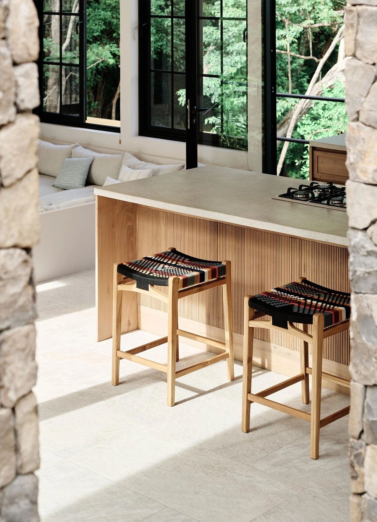 Modern kitchen with stone walls, a wooden island, and solid teak stools with woven rope seats.