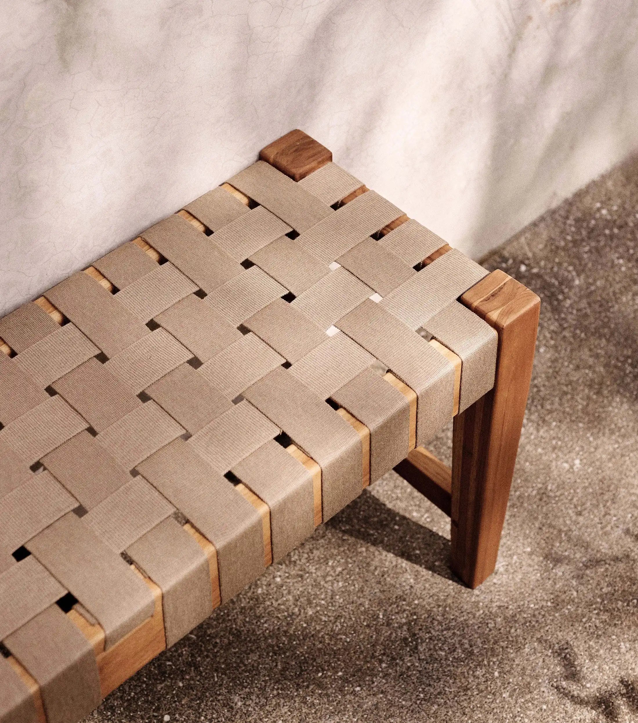 Woven strap bench with wooden teak frame on a concrete floor